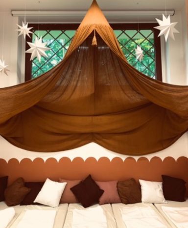 Braunfarbener Baldachin hängt über einem Bett mit weißen und braunen Kissen. Sternenlichter dekoriere.