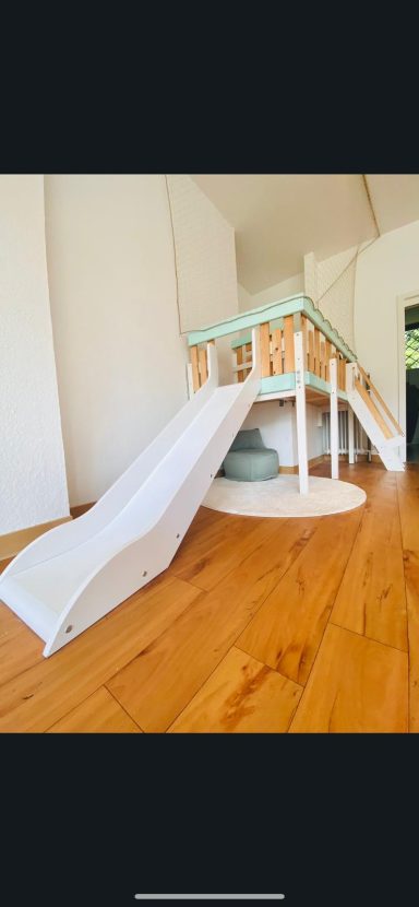 Spielplatz mit einer Rutsche und einem Spielhaus auf einem Holzboden.