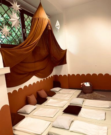 Ruhebereich mit Matten, braunen Kissen und einem dekorativen Vorhang.