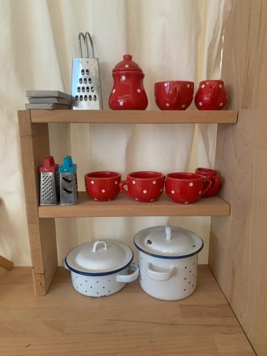 Regal mit rotem Geschirr, Gewürzbehältern und zwei weißen Kochtöpfen.